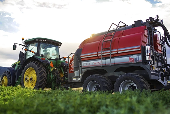 Staheli West 632 hay steamer connected to a tractor in a green field at sunset.