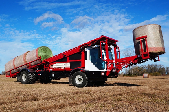 Stinger 6500 hauling a full load of square bales across a field at sunset.