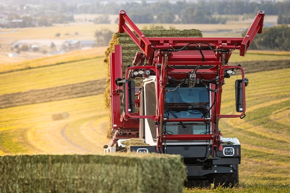 Stinger 8500 collecting hay bales in a rolling field landscape.