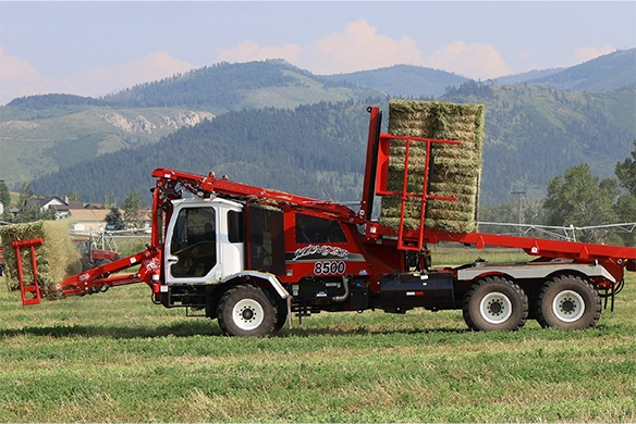 Side view of the Stinger 8500 mid-load, lifting square hay bales in the field.