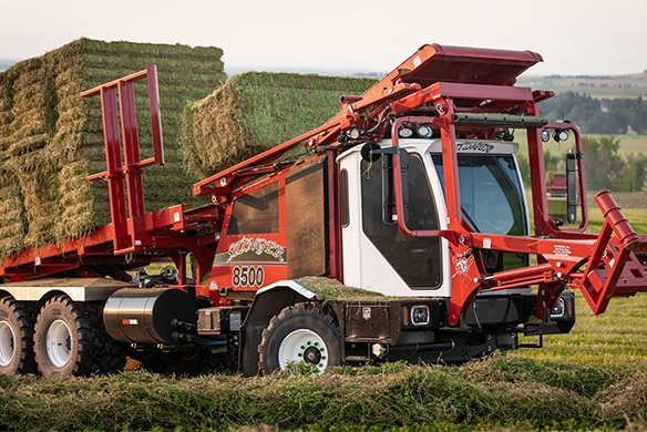Stinger 8500 stacking and hauling large square hay bales with precision in the field.