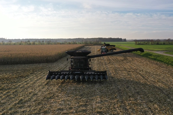 Combine with Geringhoff corn head harvesting corn, unloading into a grain cart in a wide-open field under clear skies.
