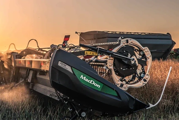 MacDon FD2 Series FlexDraper header harvesting at sunset with a combine in the background.