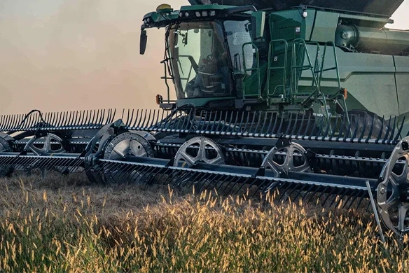 Green combine operating a MacDon header through tall field crops.