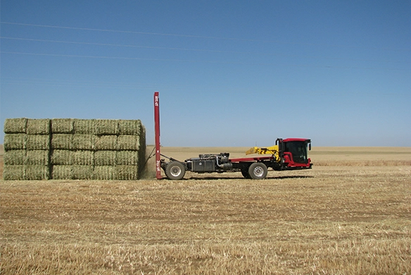 Wide side shot of Mil-Stak bale stacker lifting hay with a tractor in the foreground.