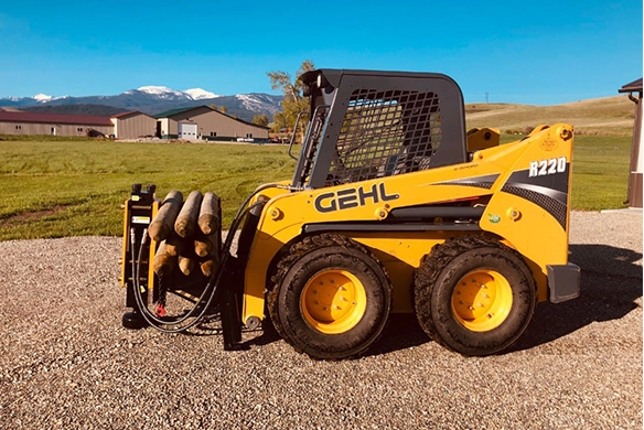 Side view of 1000E Montana Post Driver on a GEHL skid steer holding logs.