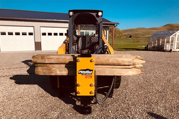 Front view of GEHL skid steer carrying stacked fence posts using the Montana Post Driver 1000E.