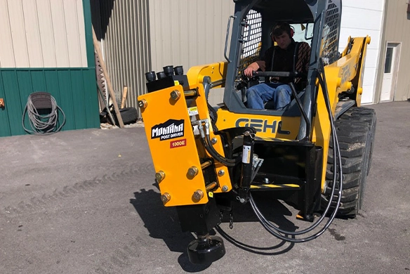 Operator seated in a skid steer with Montana Post Driver 1000E attached, ready for use.