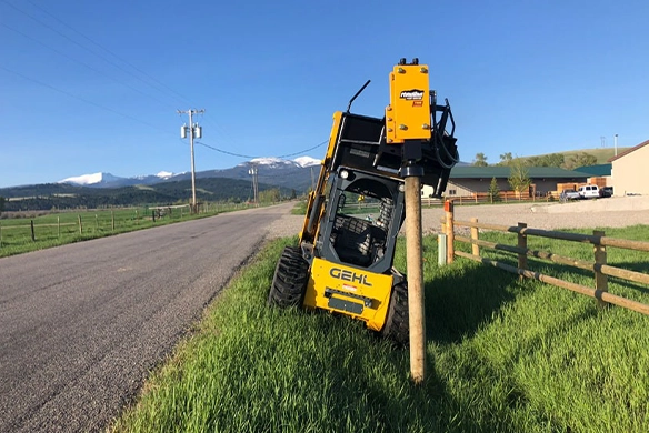 Side view of Montana Post Driver 750R on a GEHL skid steer installing a fence post.