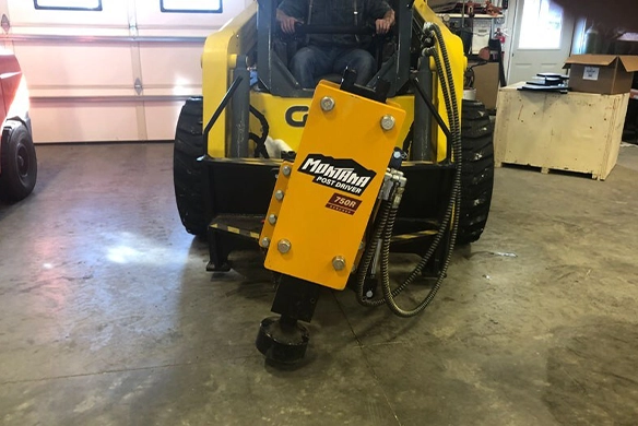 Montana Post Driver 750R positioned indoors, mounted on a skid steer.