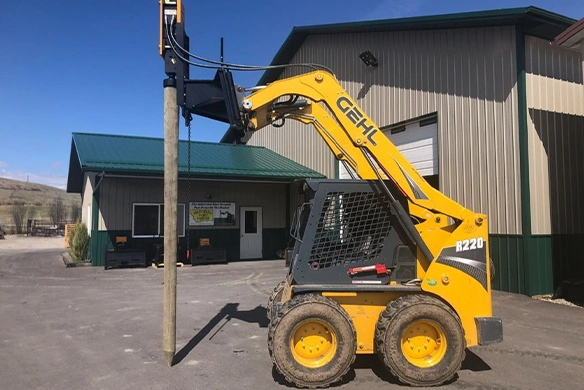GEHL R220 skid steer holding a post vertically with Montana Post Driver 750R.