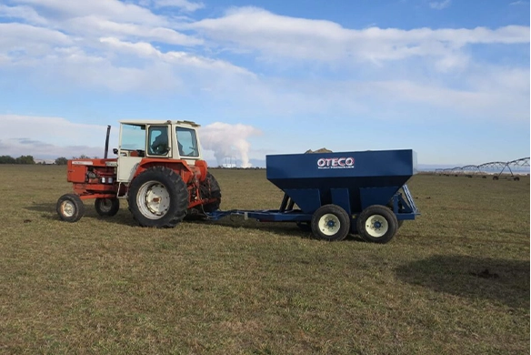 Side view of OTECO track filler trailer pulled by tractor on grass field