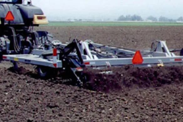 Wilcox finishing chisel with reel attachment pulled by tractor, refining soil structure for optimal planting conditions in large-scale farming operations.