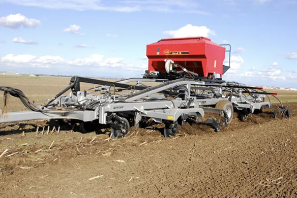 Wilcox Eliminator tillage tool with mounted seeder operating in field, combining soil preparation, residue management, and planting in a single pass.
