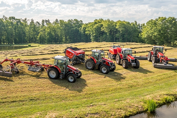Lineup of Massey Ferguson S Series tractors with hay tools including rakes, balers, and mowers in a cut field near a pond.
