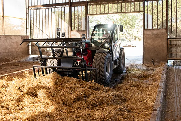 Manitou agricultural telehandler using a material handling attachment to move bedding inside a livestock facility