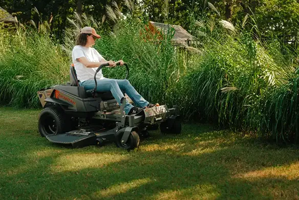 Homeowner operating a Spartan Shield HD zero-turn mower while cutting tall grass on a residential property