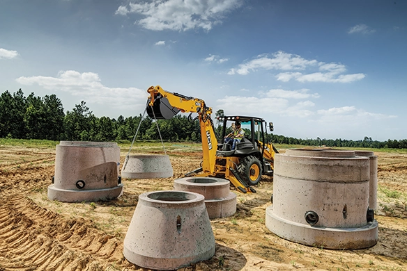 JCB 3CX backhoe loader positioning concrete chambers on a utility installation site
