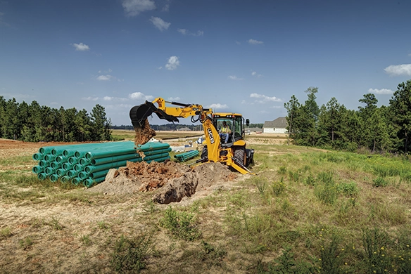 JCB 3CX backhoe loader digging and handling soil near uninstalled drainage pipes