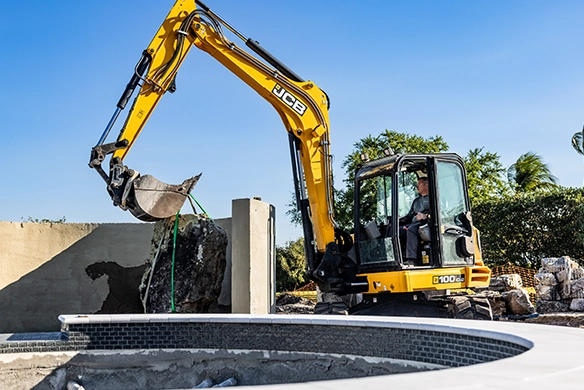 JCB 100Z-1 mini excavator lifting a large concrete section during groundworks on a residential construction site