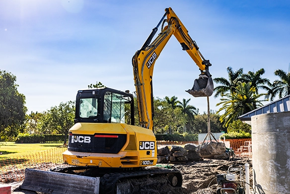 Rear three-quarter view of JCB 100Z-1 mini excavator handling concrete during outdoor groundworks