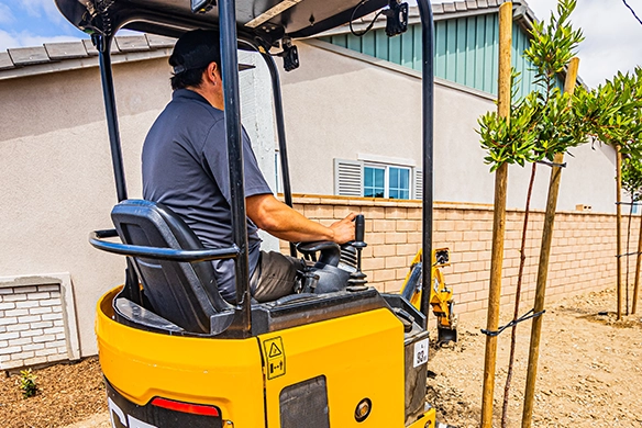 Operator using a JCB 18Z-1 mini excavator for precise digging in a residential construction area