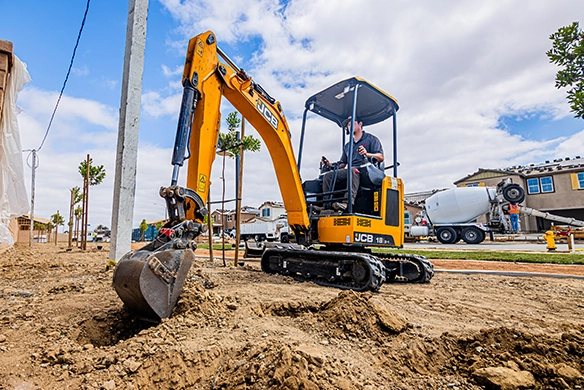 JCB 18Z-1 mini excavator digging a trench near a residential property with zero tail swing design