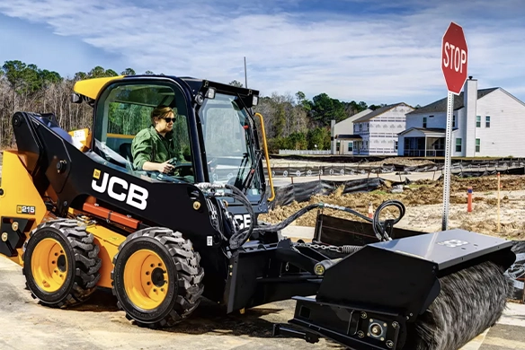 JCB 215 skid steer loader operating a road sweeper attachment on a residential construction site