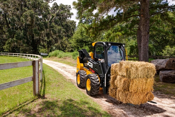 JCB 270 skid steer loader transporting stacked straw bales along a farm track