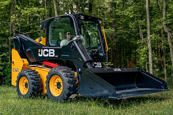 Operator handling a JCB 270 skid steer loader in a wooded area