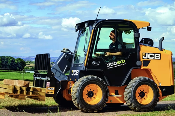 JCB 300 ECO skid steer loader using pallet fork attachment for material handling on a rural site