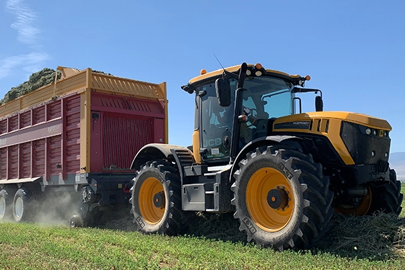 Close-up of a JCB 4000 Series agricultural tractor towing a forage wagon in the field, highlighting durability and traction during harvesting