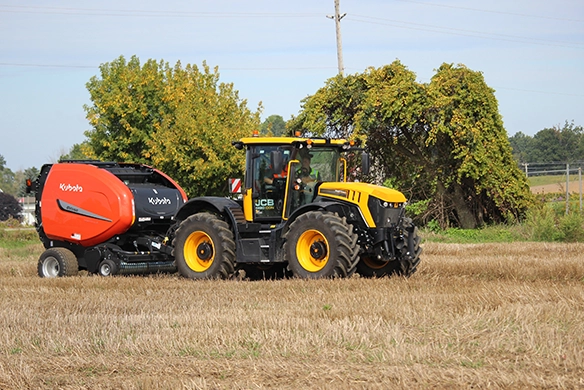 JCB 4000 Series tractor pulling a round baler in a hay field, engineered for reliable baling and livestock farming operations