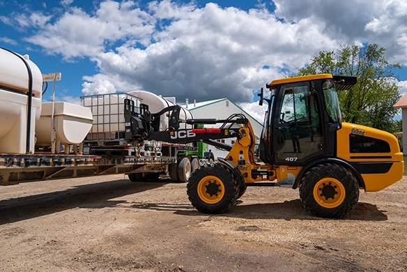 JCB 407 wheel loader at a construction site loading a flatbed trailer carrying storage tanks