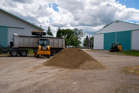 JCB 407 wheel loader positioned next to a large pile of dirt between metal warehouse buildings