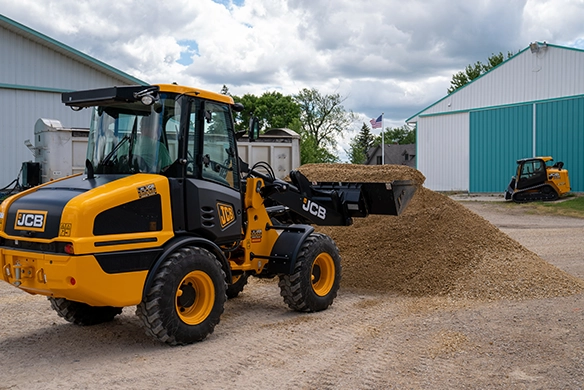 JCB 407 wheel loader with front bucket loaded with soil positioned near a pile at an industrial facility