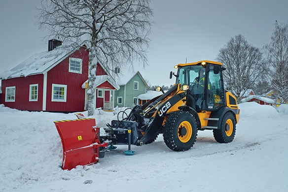 CB 409 wheel loader equipped with red snow plow attachment in front of traditional red and green Nordic-style houses