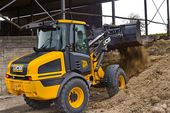 JCB 409 wheel loader dumping soil or sand from its bucket in an open-sided barn or covered work area