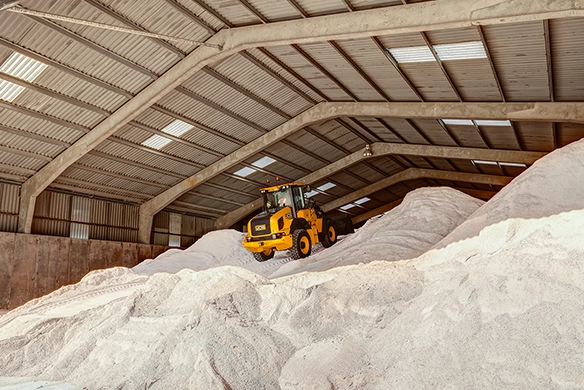 JCB 411 wheel loader working atop white sand inside a large covered warehouse with skylights