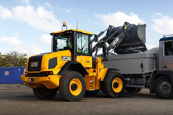 JCB 411 wheel loader dumping material into a dump truck at an outdoor work site