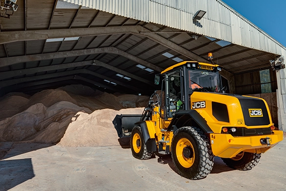 JCB 411 wheel loader beside mounds of brown material in a covered storage area