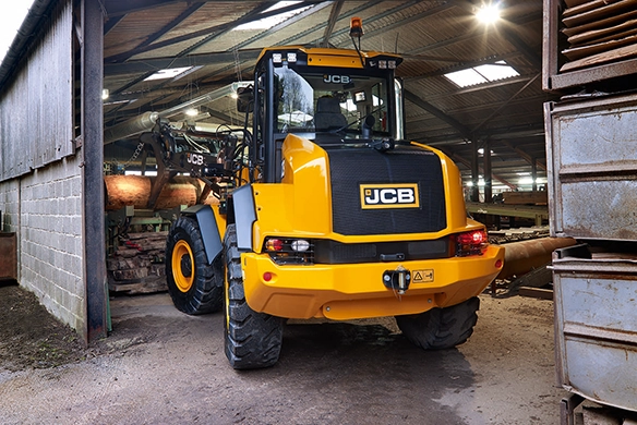 Rear three-quarter view of JCB 417 wheel loader with illuminated work lights inside an industrial sawmill building
