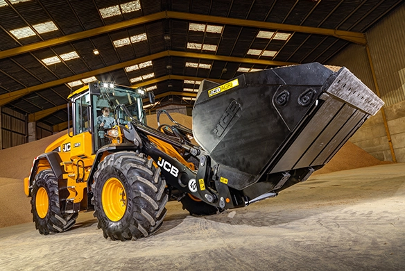 Close up image of JCB 427 Agri wheel loader with high-tip bucket loading bulk material in an agricultural warehouse