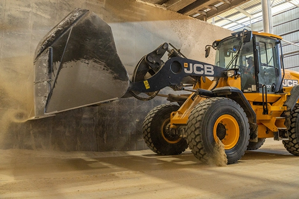 JCB 437 wheel loader tipping material from raised bucket inside an industrial storage building