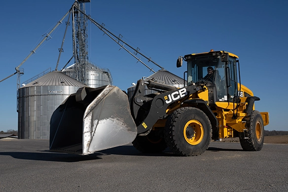 JCB 437 wheel loader with high-capacity bucket parked near grain silos on a farm site