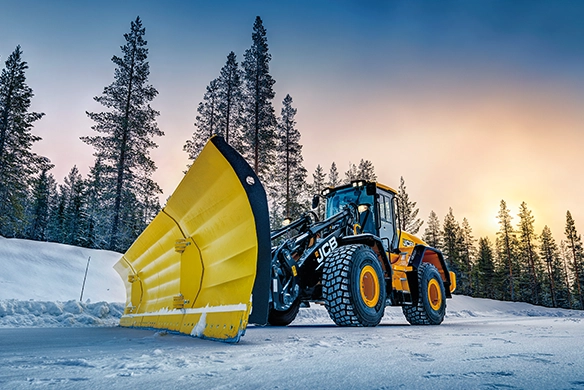JCB 457S wheel loader fitted with large snow plough clearing a snow-covered road in winter conditions