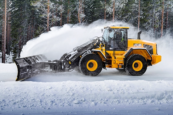 JCB 457S wheel loader pushing snow with front-mounted plough on an icy forest road