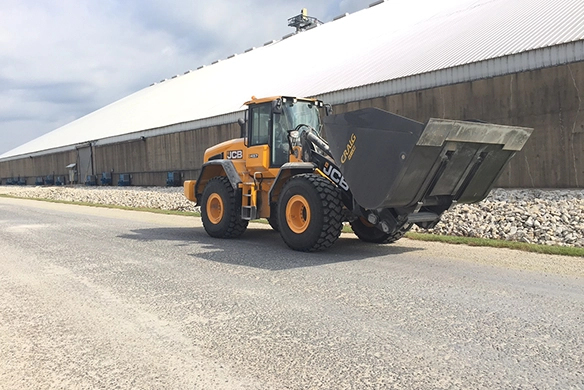 JCB 457S wheel loader carrying a large rehandling bucket outside an industrial building