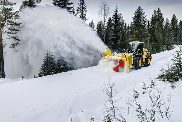 JCB 457S wheel loader fitted with high-capacity snow blower clearing deep snow in a forest environment