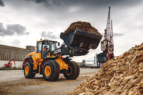 JCB 457S wheel loader lifting a full bucket of woodchip at an industrial handling site